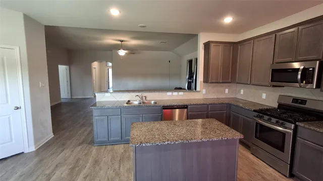 a kitchen with kitchen island granite countertop a sink stove and wooden cabinets