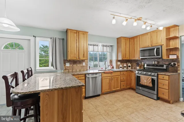 a kitchen with stainless steel appliances granite countertop a stove top oven a sink dishwasher a dining table and chairs with wooden floor