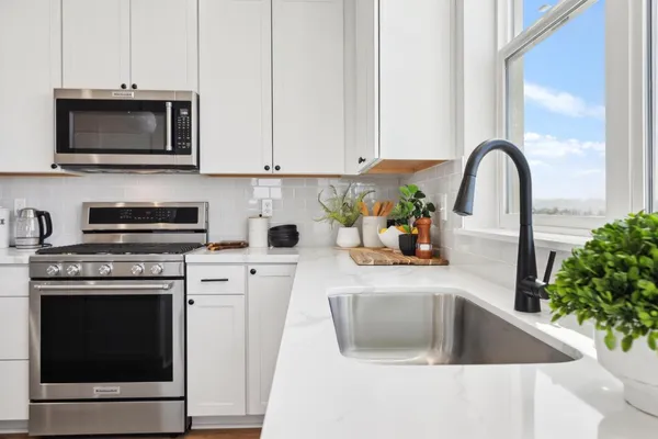 a kitchen with stainless steel appliances granite countertop a sink a microwave stove and white cabinets with wooden floor