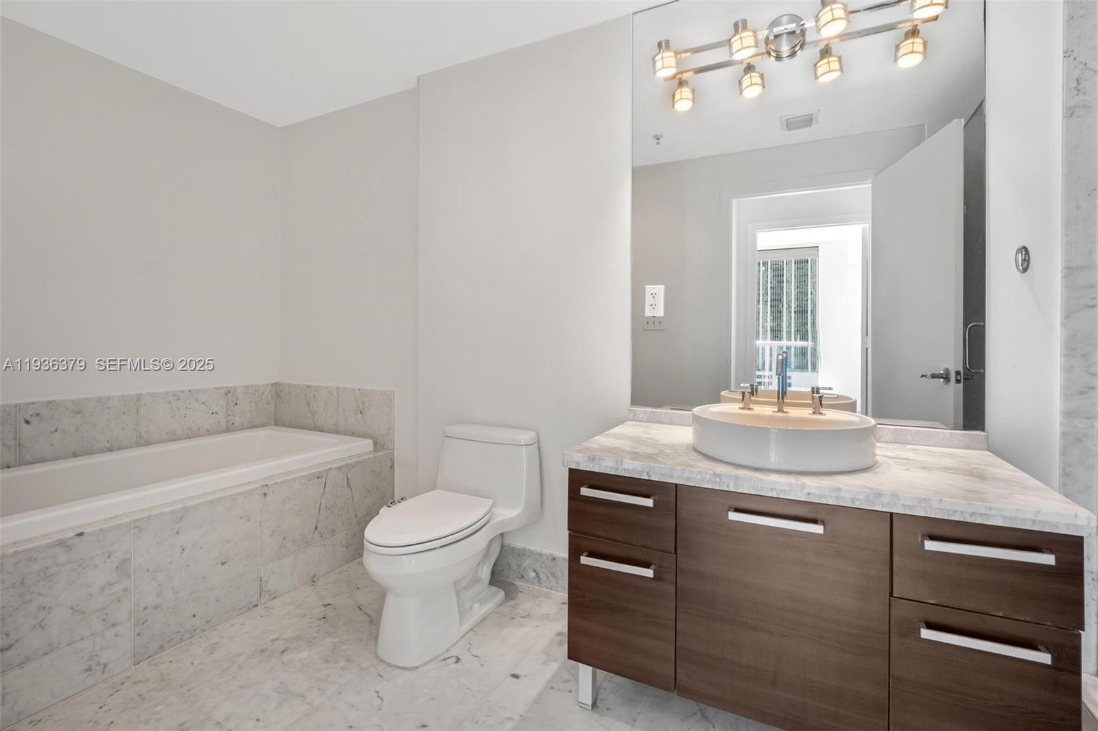 244 Biscayne Boulevard, Unit 1505 Miami, FL 33132 - Photo 15 of 25 a bathroom with a granite countertop sink a toilet a mirror and bathtub