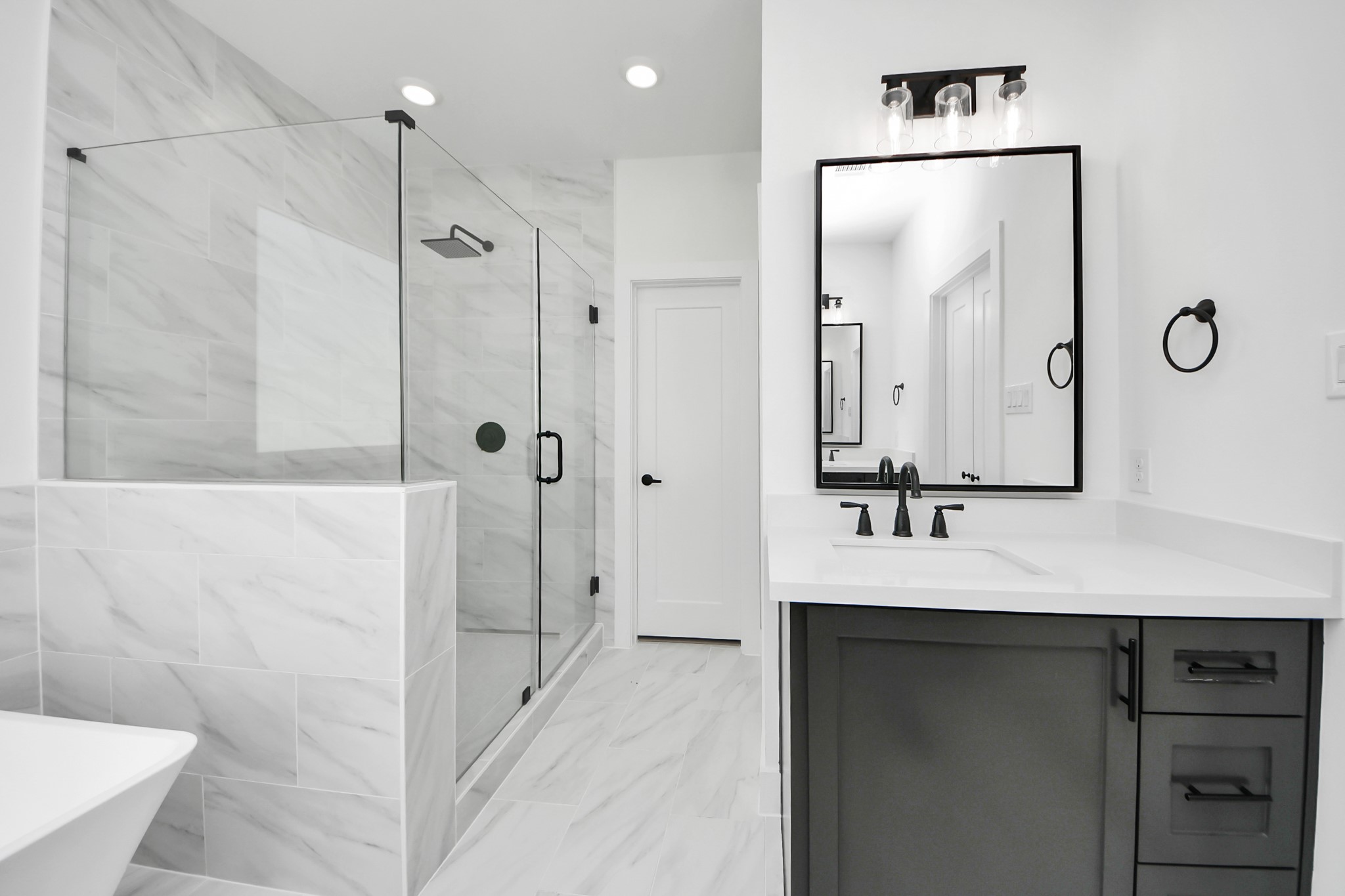 723 Marcella Street, Unit B Houston, TX 77091 - Photo 17 of 22 This bathroom features a modern design with a spacious glass-enclosed shower, large wall tiles, and a sleek vanity with a black-framed mirror. The neutral color palette and stylish fixtures create a clean, contemporary look.