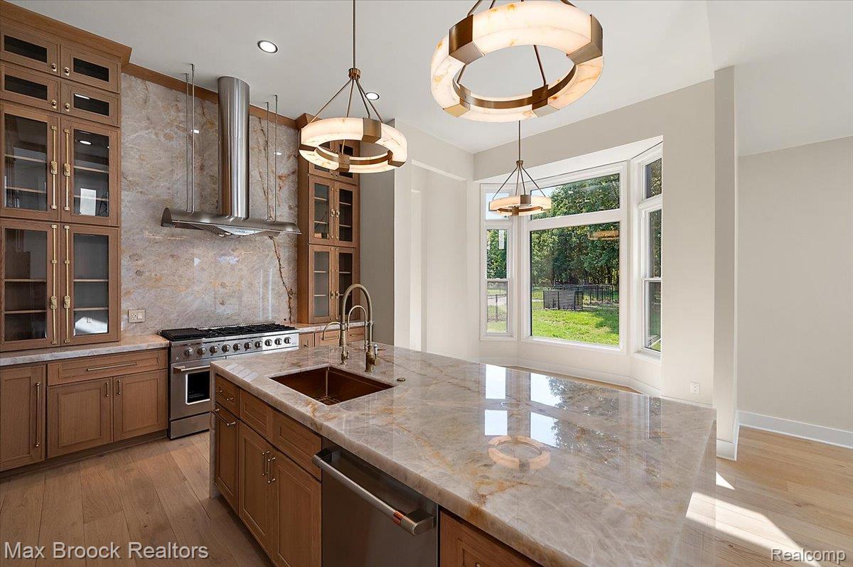 4597 Clarkston Road Clarkston, MI 48348 - Photo 17 of 74 Central island with integrated sink, stainless steel appliances, wood-finish flooring, bay window, and custom cabinetry with glass inserts