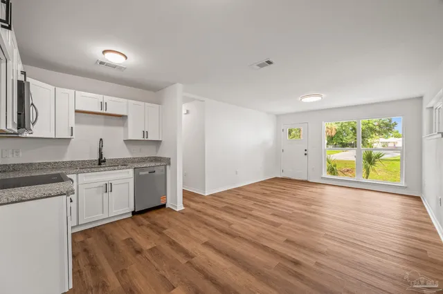 a kitchen with granite countertop a stove a sink and white cabinets with wooden floor