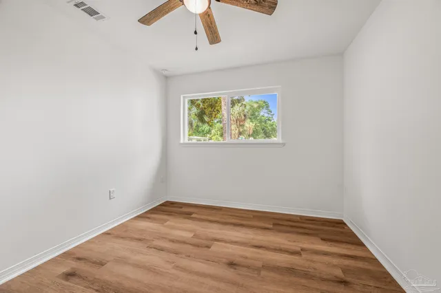 an empty room with wooden floor fan and windows