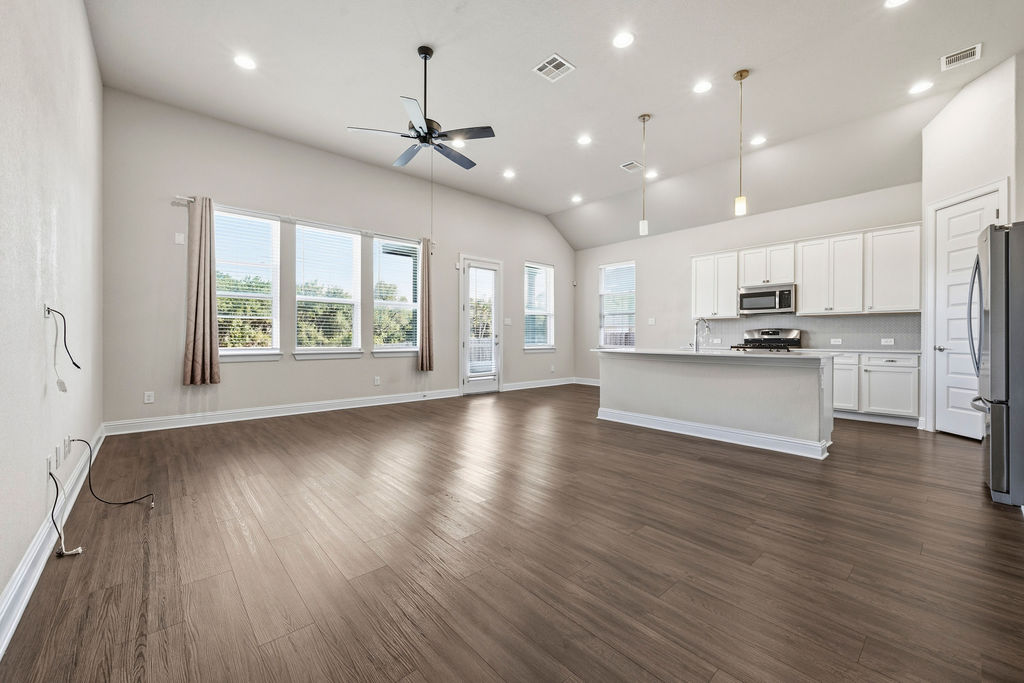 2032 Base Burner Path Leander, TX 78641 - Photo 10 of 34 Spacious open-concept living area featuring wood-finish flooring, vaulted ceilings with recessed lighting, and a modern kitchen with white cabinetry and stainless steel appliances