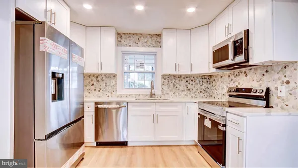 a kitchen with stainless steel appliances a stove top oven a sink a refrigerator white cabinets and wooden floor