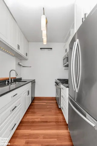 a view of empty room with wooden floor and kitchen