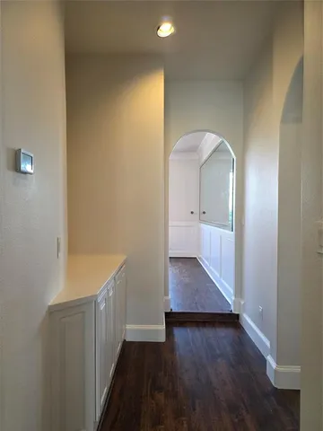 a view of a hallway to an empty room with wooden floor and a bathroom