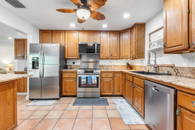 a kitchen with stainless steel appliances granite countertop a refrigerator a sink dishwasher a stove with wooden cabinets and floor