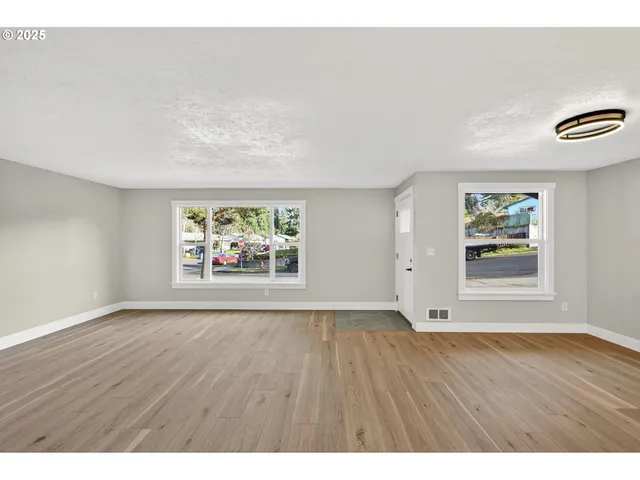 a view of an empty room with a window and wooden floor