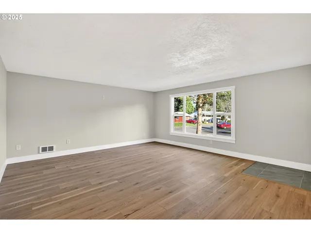a view of an empty room with window and wooden floor