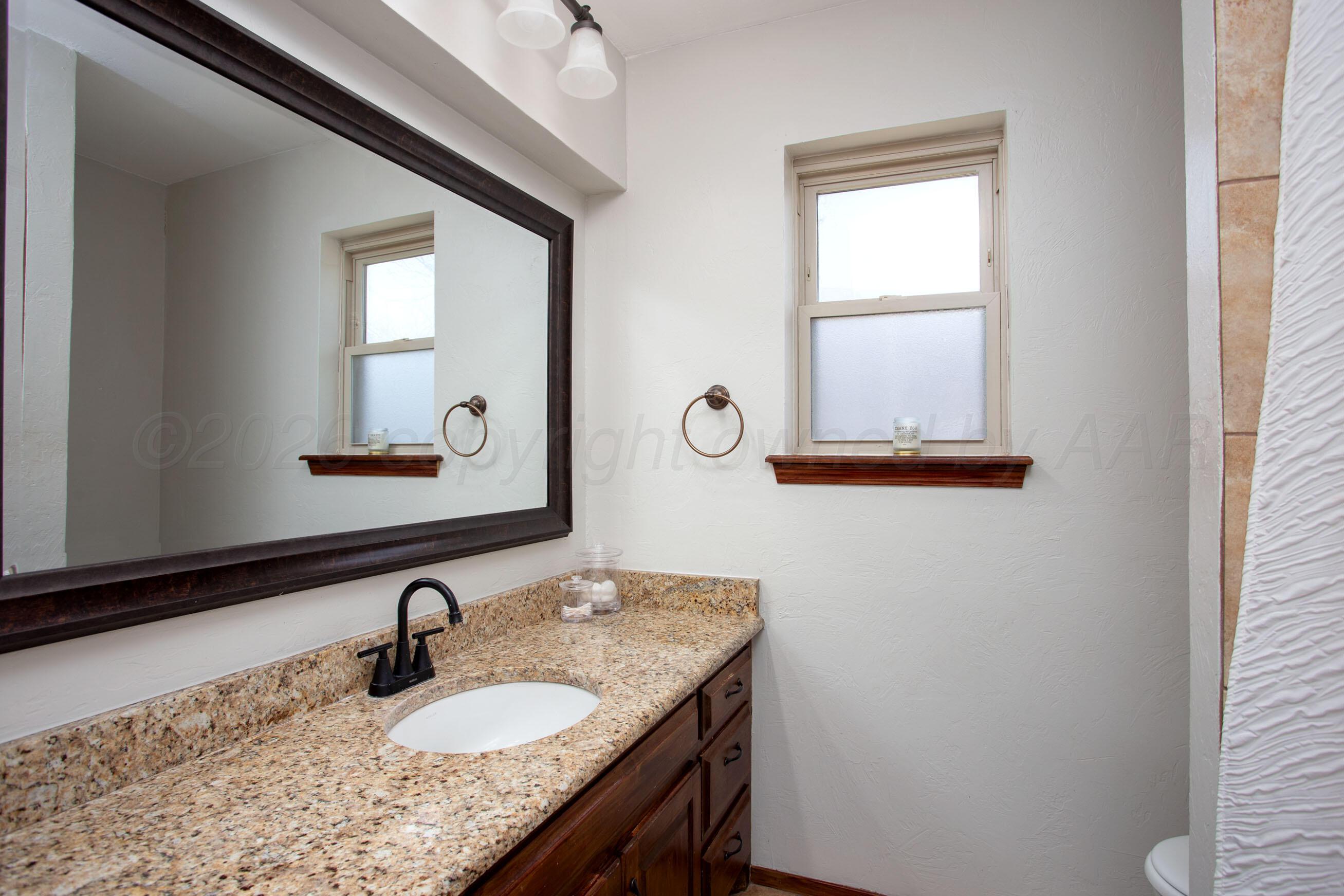 7924 Simpson Drive Amarillo, TX 79121 - Photo 20 of 33 a bathroom with a granite countertop sink a mirror and window