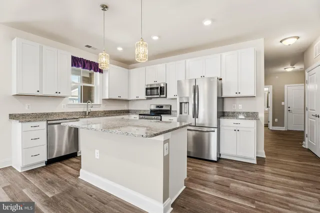 a kitchen with stainless steel appliances granite countertop a refrigerator a stove a sink and white cabinets