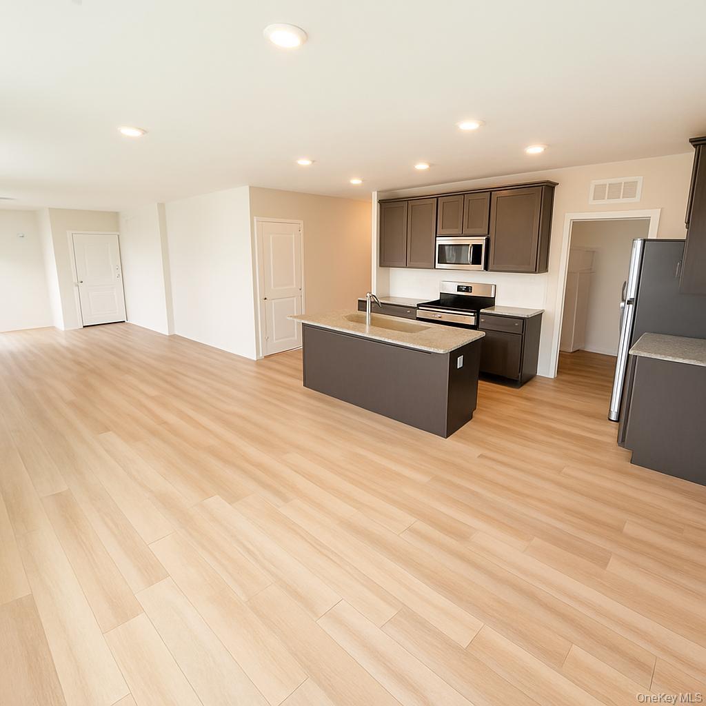 a large kitchen with stainless steel appliances kitchen island a large counter top and a stove top oven with wooden floor