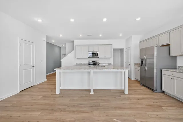 a large white kitchen with wooden floor and stainless steel appliances
