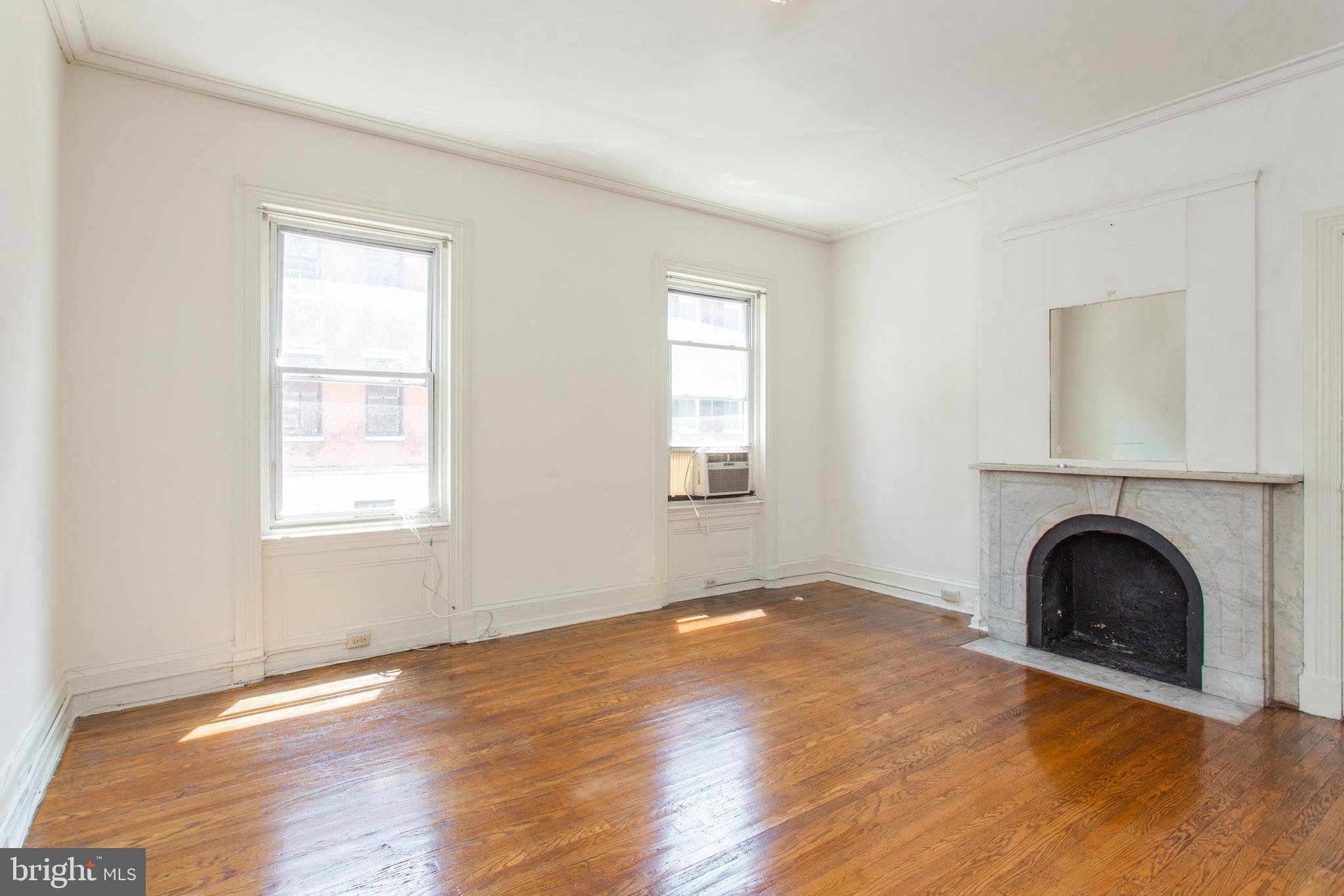 1807 Spruce Street, Unit 2F Philadelphia, PA 19103 - Photo 2 of 17 an empty room with windows a fireplace and wooden floor