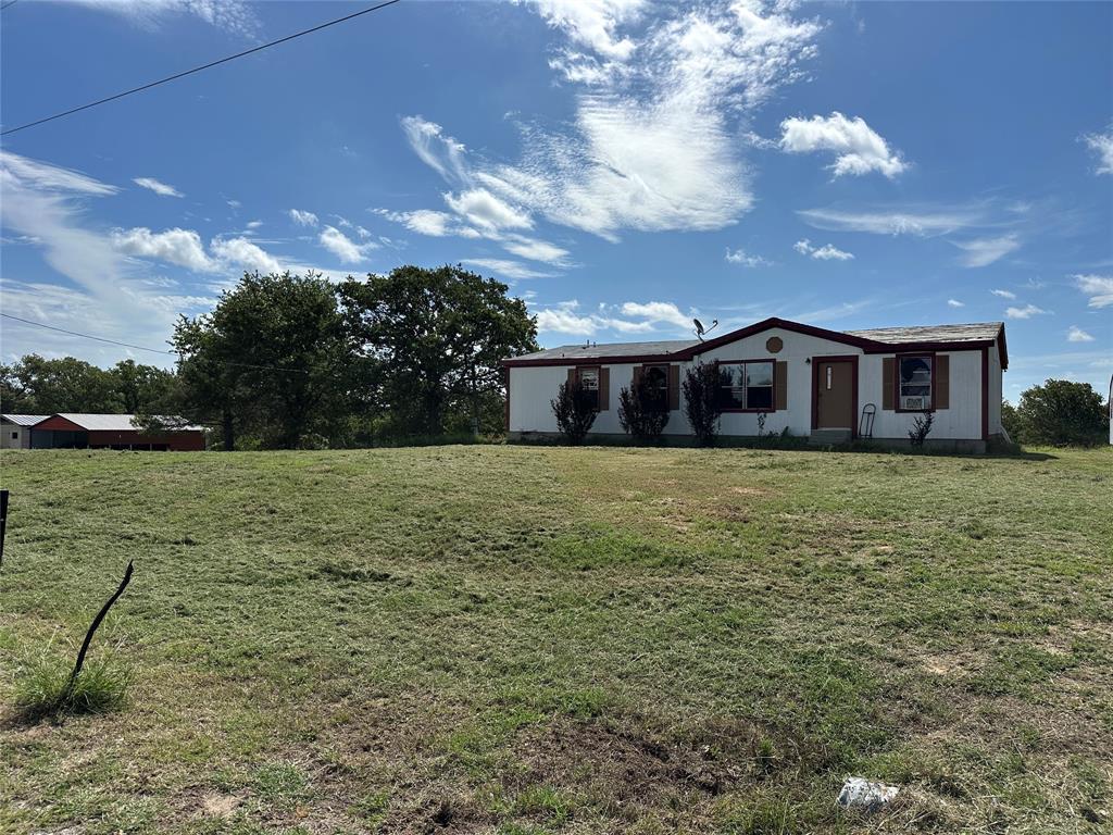 570 Big Salty Lane Springtown, TX 76082 - Photo 16 of 36 Spacious lot with a white single-story residence featuring a brown trim roof, multiple windows with brown shutters, and a front entry door