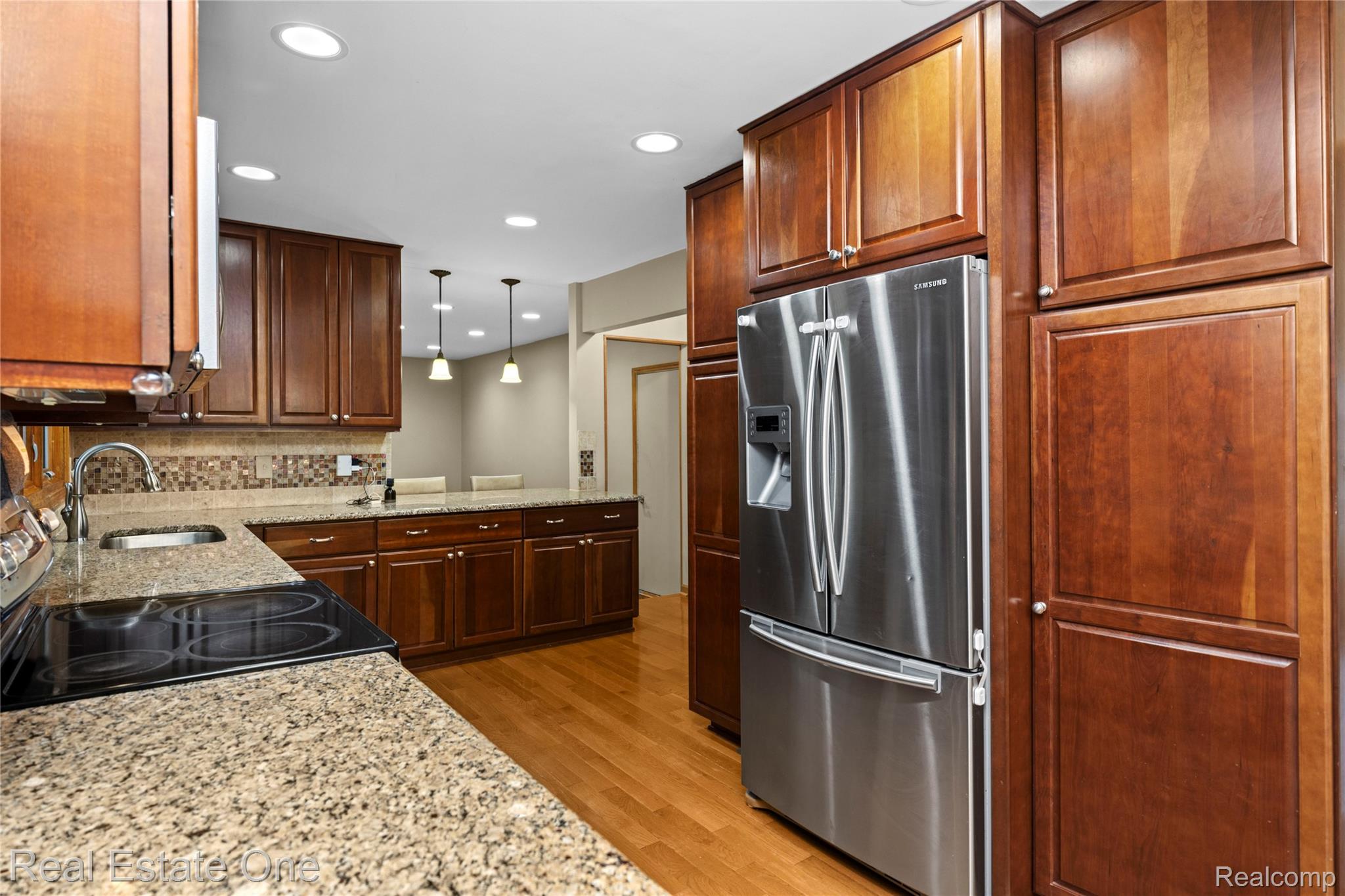 39750 Cheviot Road Canton, MI 48188 - Photo 17 of 71 Chef's kitchen featuring rich wood cabinetry, granite countertops, stainless steel French-door refrigerator, gas cooktop with tile backsplash, recessed lighting, and warm wood-finish flooring throughout the open layout