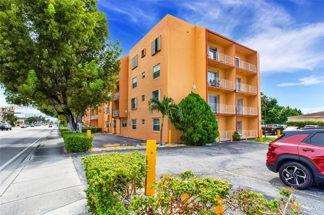 a front view of a building with garden and trees