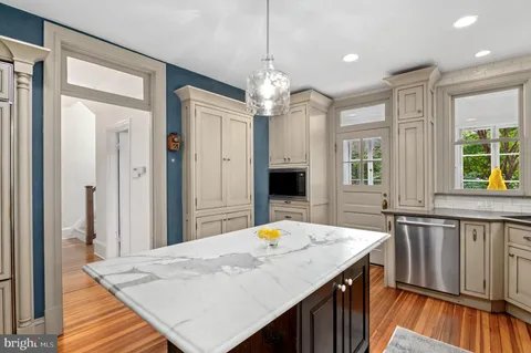 a kitchen with stainless steel appliances kitchen island granite countertop a refrigerator a sink dishwasher a dining table and chairs with wooden floor