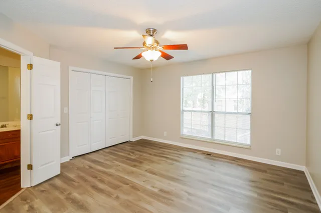 an empty room with wooden floor fan and windows