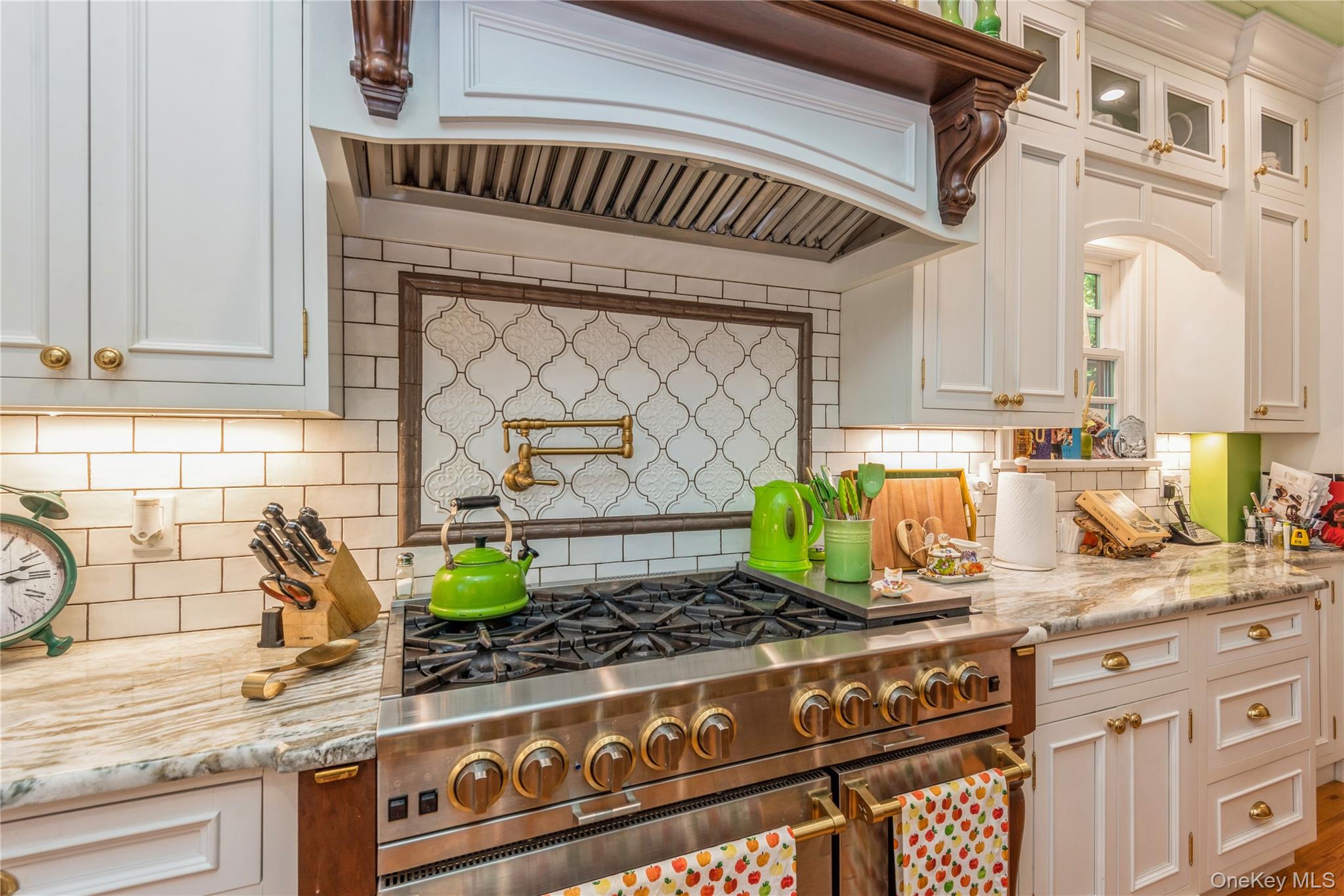 110 Red Spring Lane Glen Cove, NY 11542 - Photo 22 of 43 Professional-grade stainless steel range with brass-tone accents, set against a subway tile backsplash featuring an arabesque-patterned inset and a wall-mounted pot filler