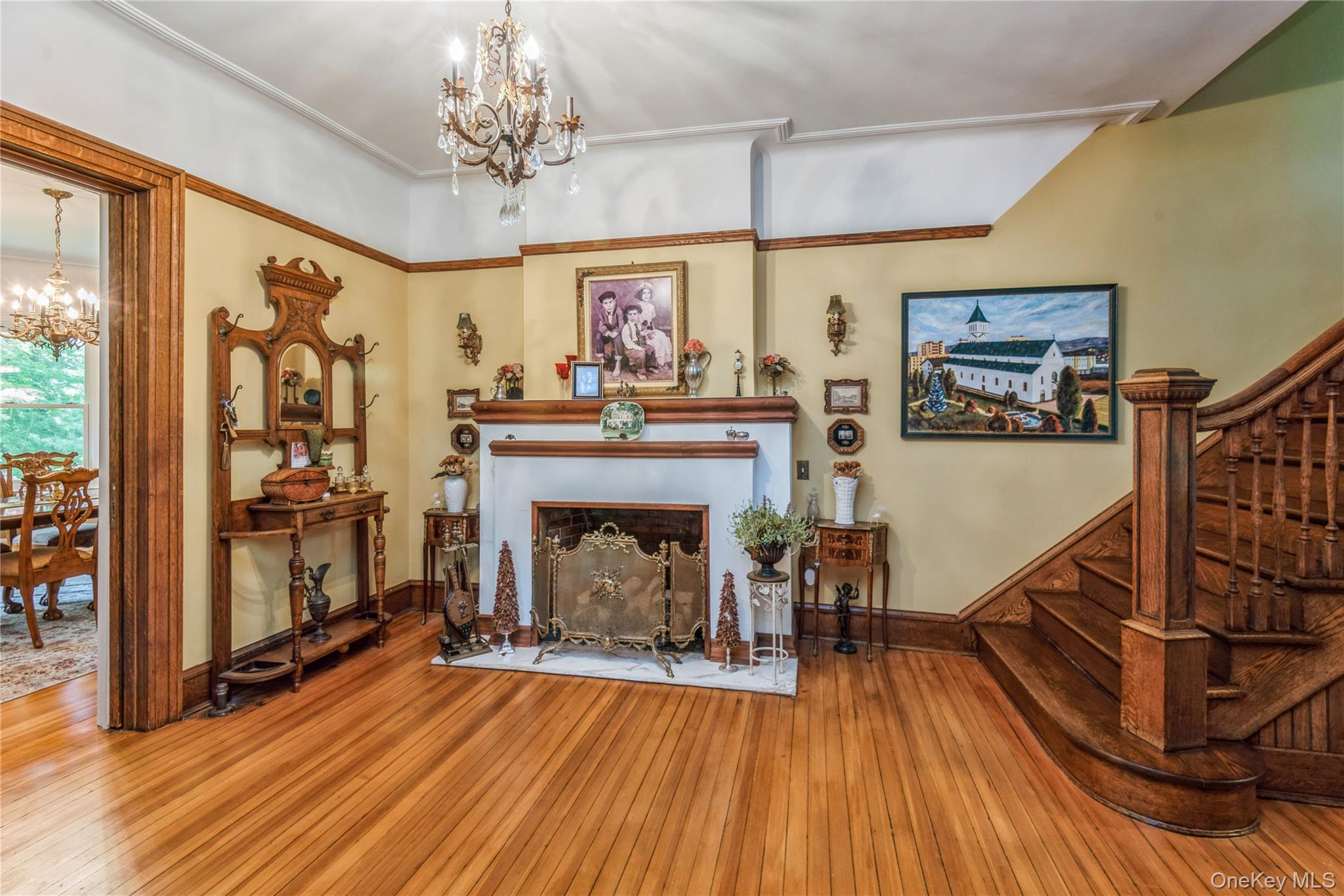 110 Red Spring Lane Glen Cove, NY 11542 - Photo 9 of 43 Spacious entry hall featuring wood-finish flooring, a decorative fireplace with a mantel, a chandelier, and an intricately carved wooden staircase