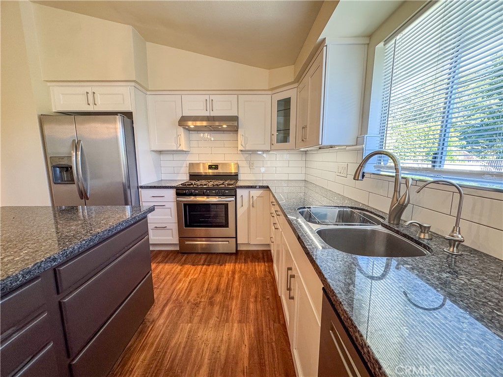 12162 Bradford Place Granada Hills, CA 91344 - Photo 7 of 27 a kitchen with granite countertop stainless steel appliances a sink dishwasher a refrigerator oven and white cabinets with wooden floor