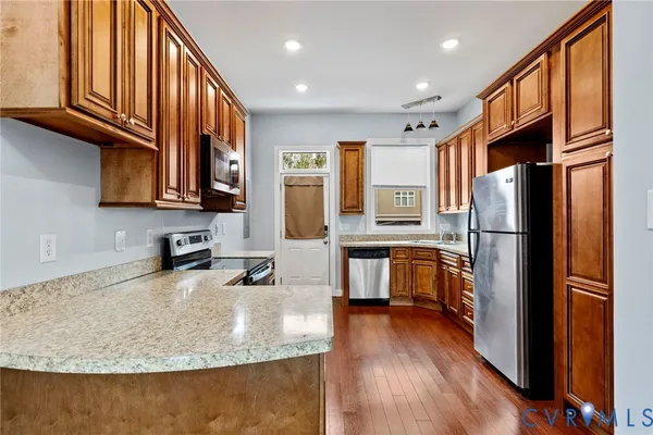 a kitchen with stainless steel appliances granite countertop a refrigerator a stove and a sink with wooden floor