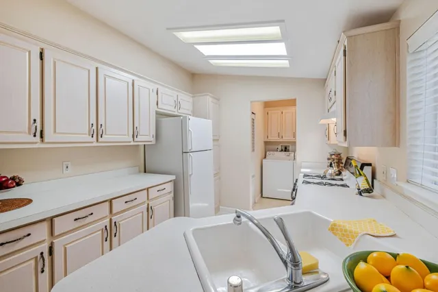 a kitchen with stainless steel appliances granite countertop a sink dishwasher a refrigerator and white cabinets with wooden floor