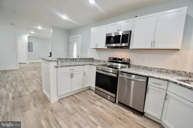 a kitchen with granite countertop white cabinets appliances a sink and a window