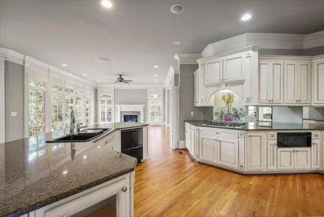 a kitchen with stainless steel appliances granite countertop a stove a sink and white cabinets with wooden floor