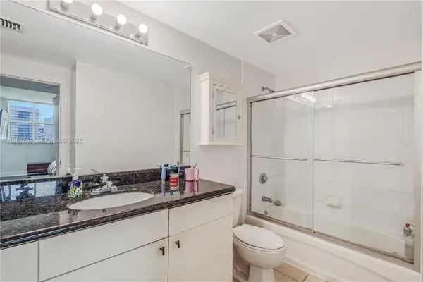 a bathroom with a granite countertop sink a toilet a mirror and shower