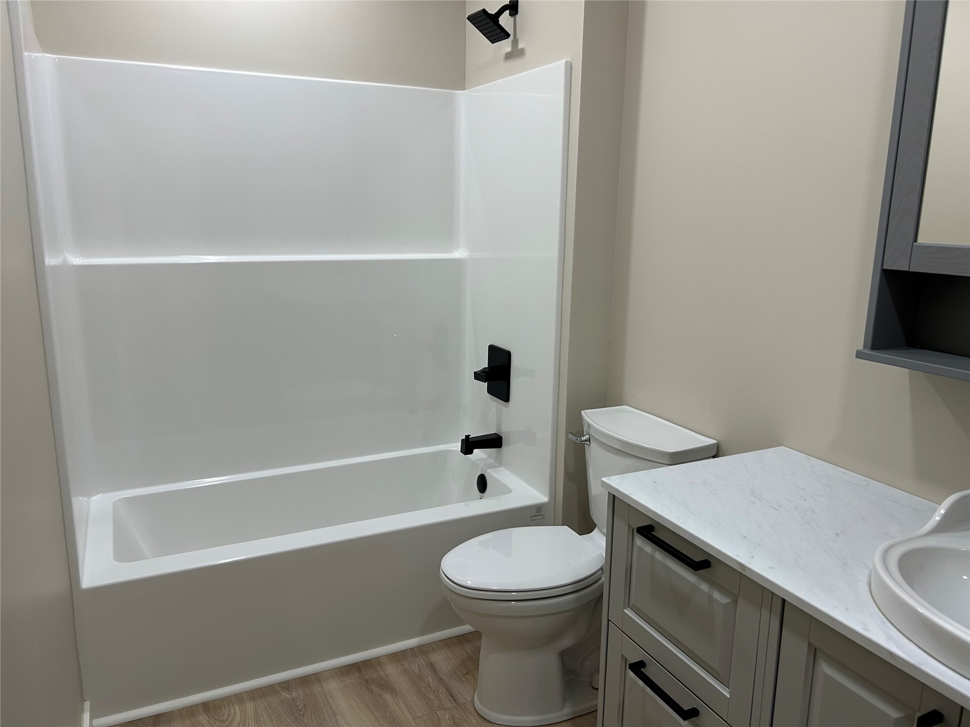 190 South 3 Mile Road Fort Gibson, OK 74434 - Photo 10 of 35 Bathtub with integrated shower, matte black fixtures, wood-finish flooring, white vanity with integrated sink, and gray wall-mounted cabinet with mirror
