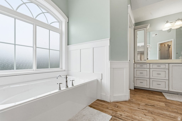 672 Perry Hollow Drive Mapleton, UT 84664 - Photo 45 of 106 Primary bath, Soaking tub with a polished chrome faucet set, featuring an arched transom window, wood-finish flooring, white wainscoting, and a vanity with multiple drawers