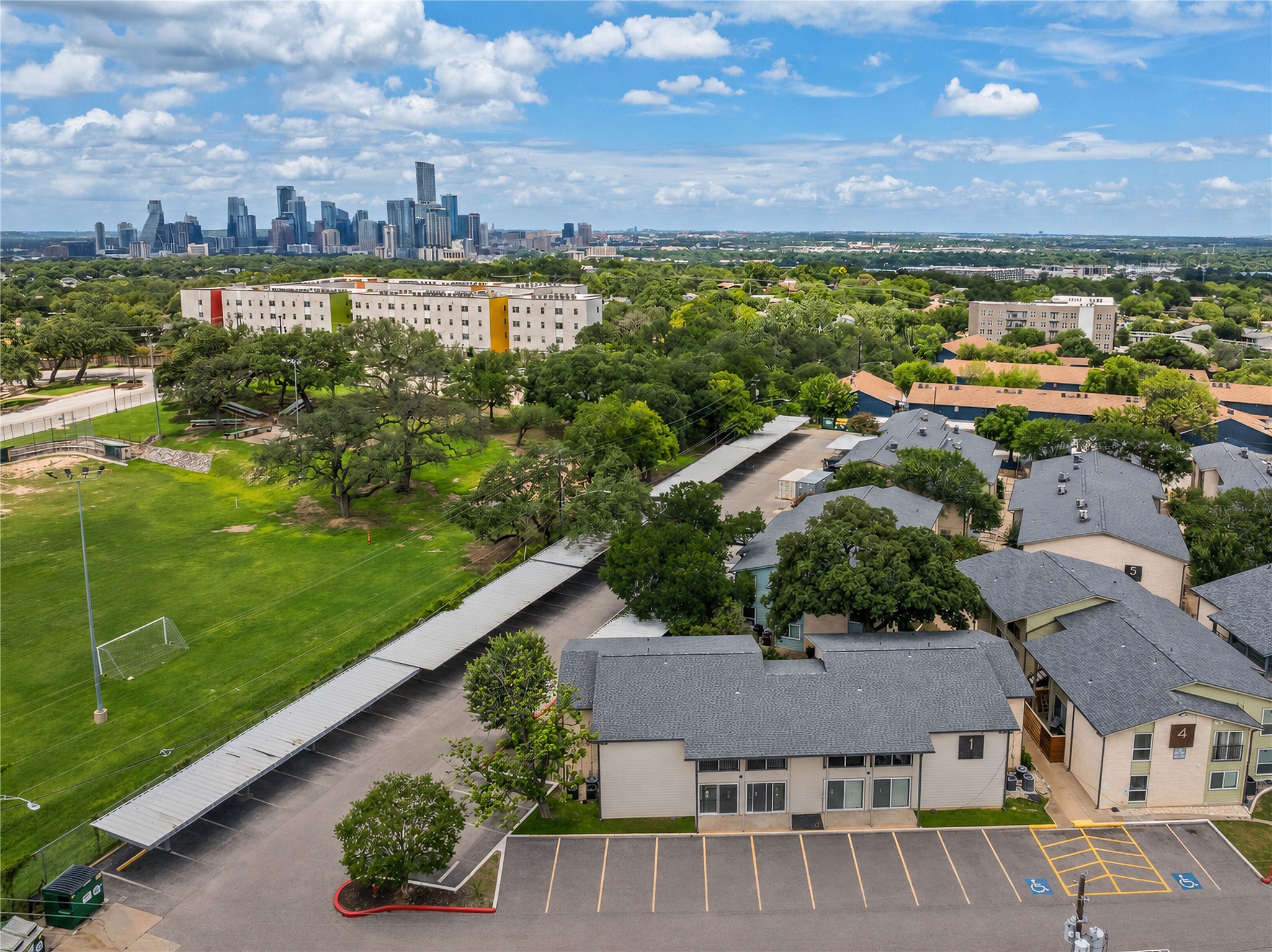 2124 Burton Drive, Unit 159 Austin, TX 78741 - Photo 22 of 23 Aerial view captures multiple residential buildings with ample parking and a city skyline backdrop.