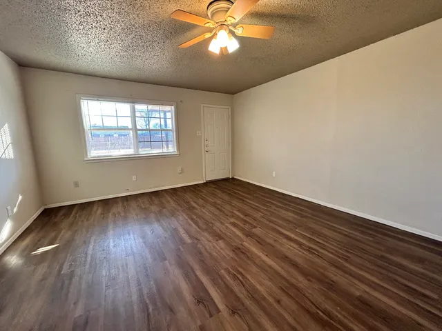 an empty room with wooden floor chandelier fan and windows