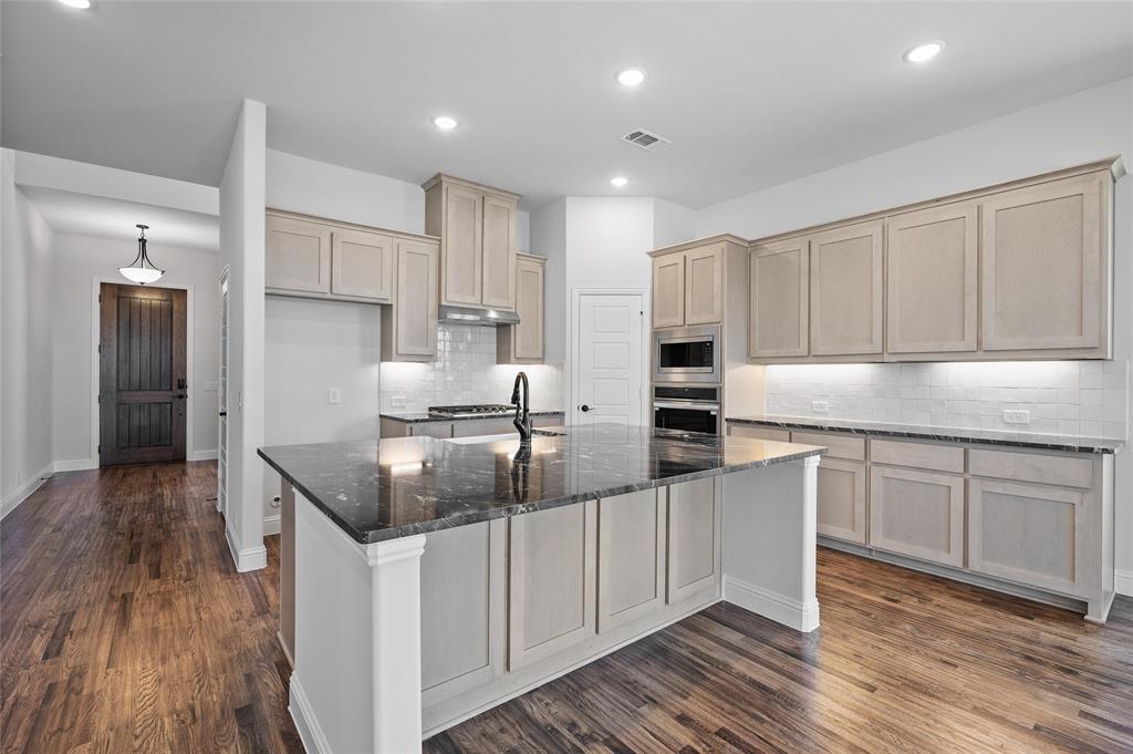 613 Brazos Drive Van Alstyne, TX 75495 - Photo 14 of 29 Kitchen featuring dark stone countertops, decorative backsplash, dark wood-type flooring, a kitchen island with sink, and appliances with stainless steel finishes