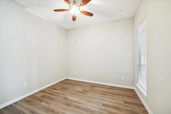 an empty room with a chandelier fan and wooden floor