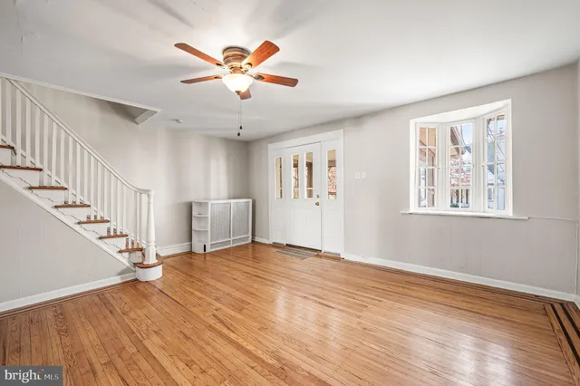 a view of an empty room with wooden floor and a ceiling fan