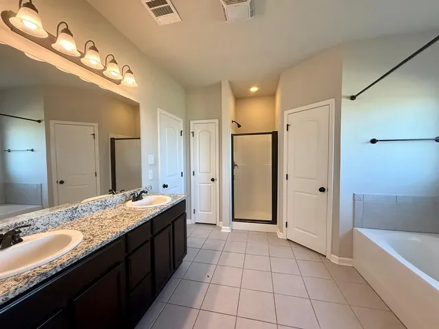 a spacious bathroom with a granite countertop double vanity sink a mirror and a bathtub