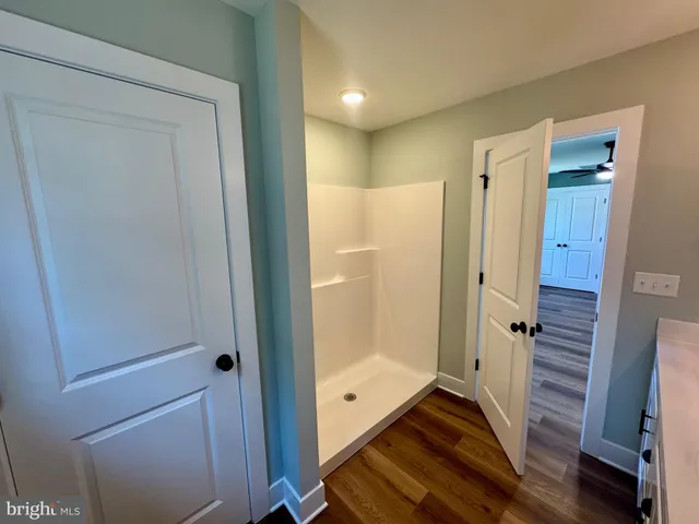 a view of an empty room with wooden floor and a ceiling fan