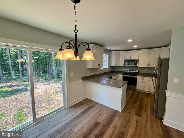 a kitchen with granite countertop a stove a sink dishwasher and white cabinets with wooden floor