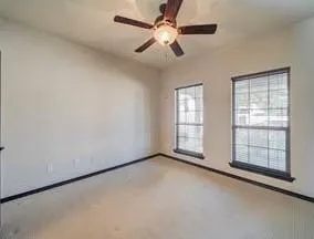 an empty room with chandelier fan and windows