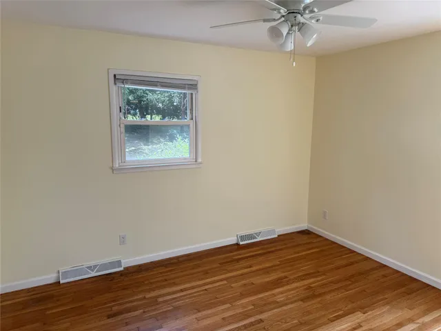 a view of an empty room with wooden floor and a fan