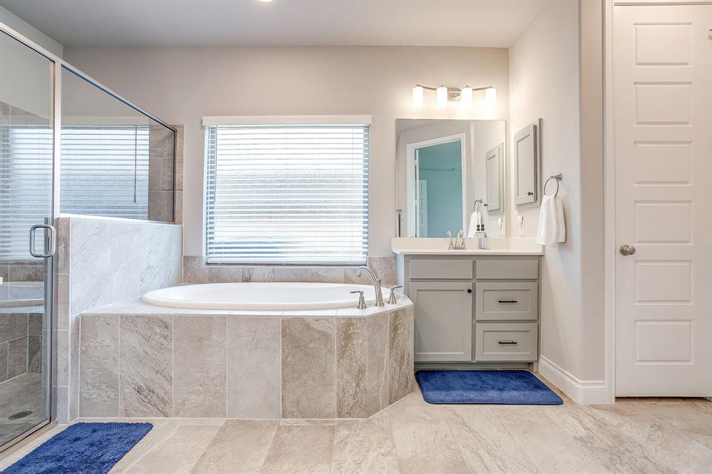 5709 Pope Creek Road Fort Worth, TX 76126 - Photo 20 of 39 Relax in this spacious primary bathroom featuring a soaking tub with surrounding stone-look tile, an adjacent glass-enclosed shower, double vanities, and separate his-and-hers walk-in closets.