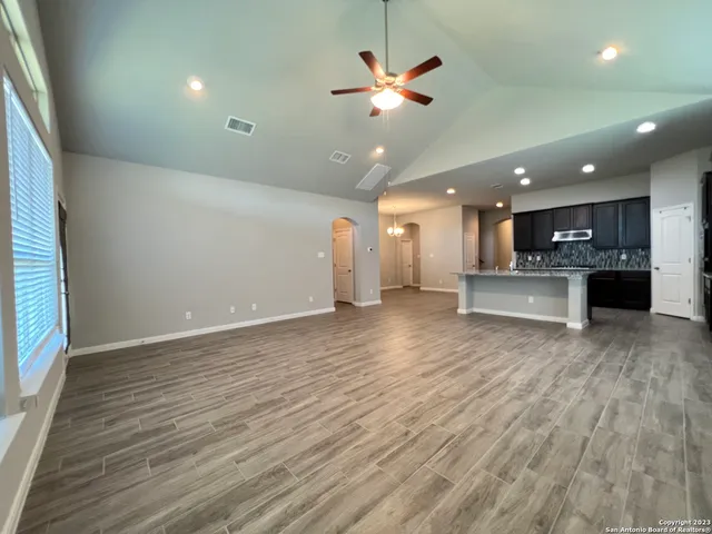 an empty room with wooden floor and kitchen view