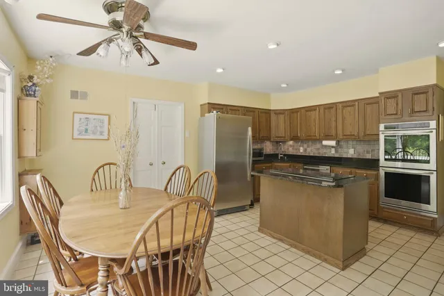 a kitchen with stainless steel appliances kitchen island granite countertop a dining table chairs and a refrigerator