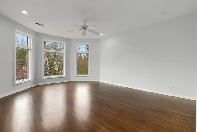 a view of an empty room with wooden floor and a ceiling fan