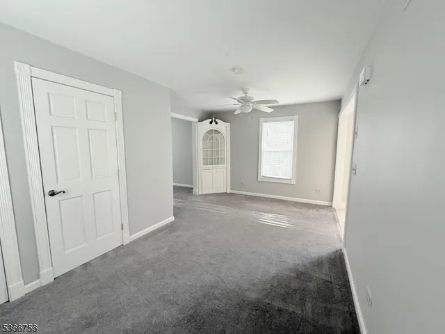 an empty room with chandelier fan and windows
